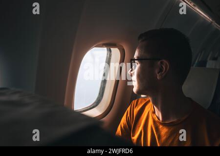 Portrait of man traveling by airplane. Passenger looking through plane window during flight. Stock Photo