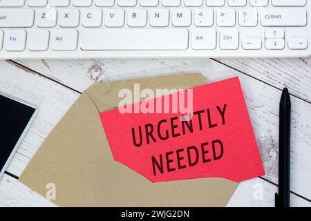 Urgently needed text on red card with envelope, white keyboard and pen. Stock Photo