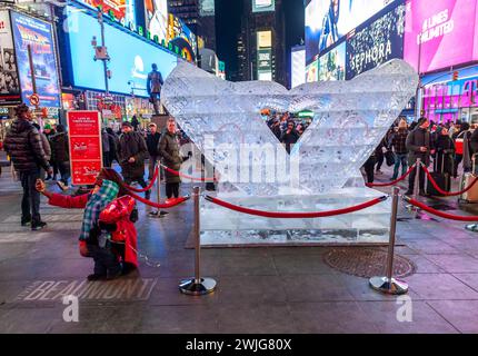 Tourists crowd Lovie Pignata’s “Smitten” ice sculpture, the winner of the Winter Ice Sculpture Show on Governor’s Island, in Times Square in New York on Valentine’s Day, Wednesday, February 14, 2024. The two mittens carved in ice forming a heart was upsized by the Okamoto Studio and will be displayed in Duffy Square until it “self-destructs” by melting. (© Richard B. Levine) Stock Photo