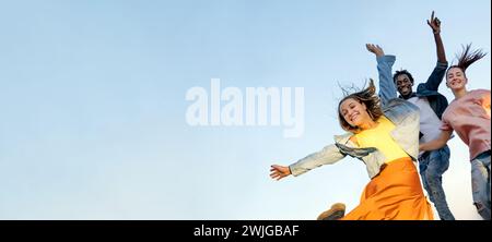 Group of young multiracial friends enjoying freedom together - Happy people jumping to blue sky background - Friendship concept Stock Photo
