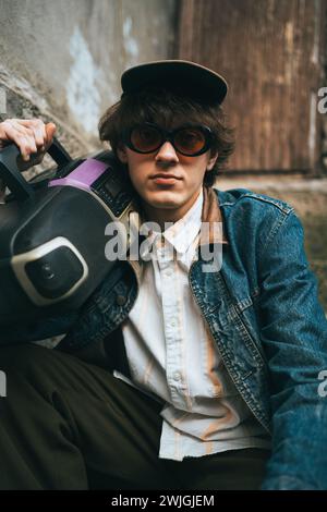 Man holding boombox on his shoulder sitting on stairs. 90s retro style nostalgia concept. Stock Photo