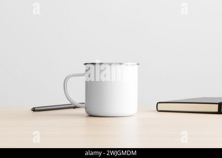 Enamel mug mockup with workspace accessories on the wooden table. Stock Photo