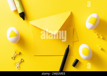 Colorful easter concept. Blank greeting card and envelope. Easter eggs,pushpins, binder clips and color pens on yellow background. Stock Photo