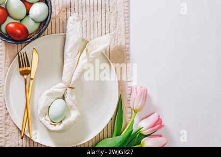 Easter table setting, with napkin folded in shape of a rabbit, blue egg and tulips, top view. Spring flat lay Stock Photo