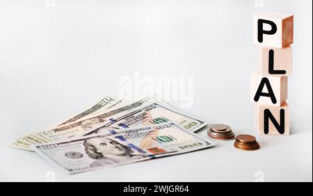 The word PLAN composed of building blocks, nearby dollars and coins isolated on a light background Stock Photo