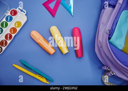 Backpack with colorful school supplies flat lay on blue background Stock Photo