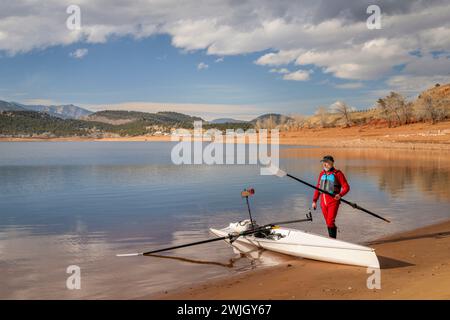senior rower is rigging his rowing shell on a shore of Carter Lake in northern Colorado in winter scenery Stock Photo