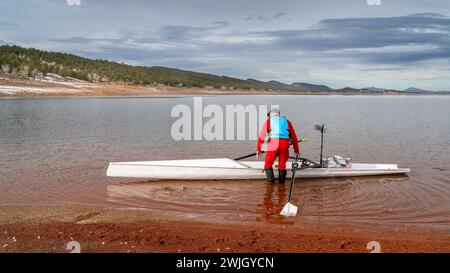 Senior male rower is launching a rowing shell on a shore of Carter Lake in northern Colorado in winter scenery. Stock Photo