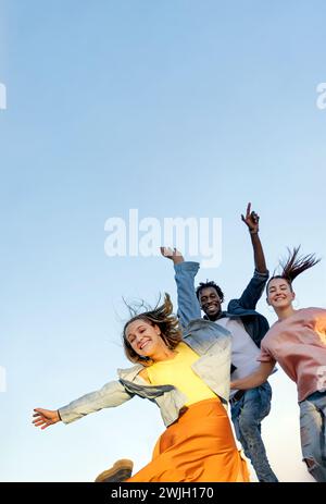 Group of young multiracial friends enjoying freedom together - Happy people jumping to blue sky background - Friendship concept Stock Photo