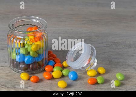 Peanuts in multi-colored glaze in a glass jar on a wooden table Stock Photo