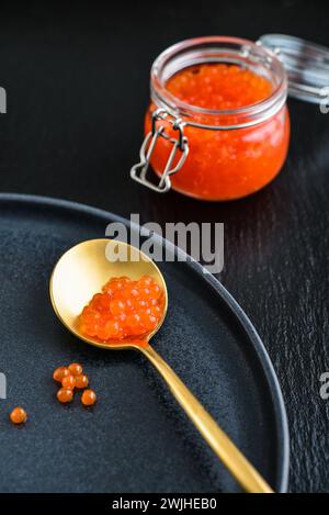 Red caviar in the glass jar on black slate  background closeup Stock Photo