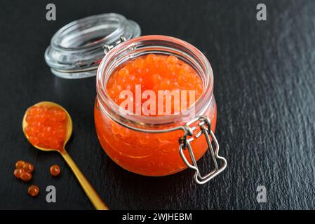 Red caviar in the glass jar on black slate  background closeup Stock Photo