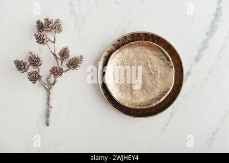 Two golden plates and a decorative golden branch with pine cones on a white marble background, top view Stock Photo