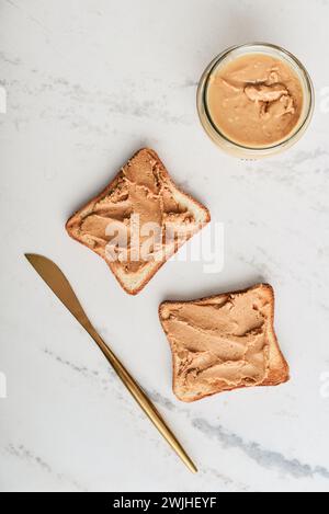 Creamy and smooth peanut butter in jar with peanut butter sandwich on marble table Stock Photo
