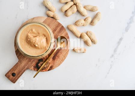 Creamy and smooth peanut butter in jar peanuts in shell on marble table. Natural nutrition and organic food. Stock Photo