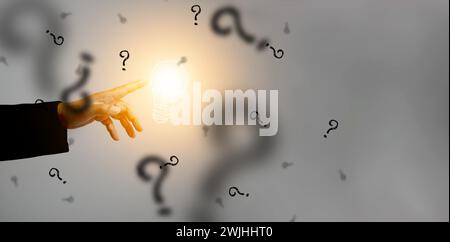Idea concept. Hand touches an illuminated light bulb surrounded by black question marks. Lightblub is on as a symbol of innovation, inspiration, solut Stock Photo