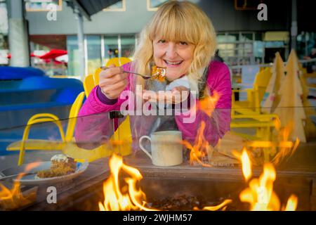 Woman enjoying coffee and eating carrot cake outdoors by warm fire in winter Stock Photo