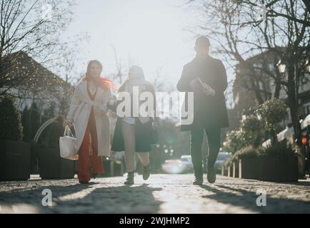 Three young people engage in a business discussion while walking in an urban setting, highlighting collaboration, diversity, and motion. Stock Photo