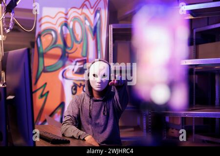 Anonymous man pointing at mobile phone camera while recording ransom video. Criminal streaming threat on smartphone while breaking law and doing illegal activity in abandoned warehouse Stock Photo