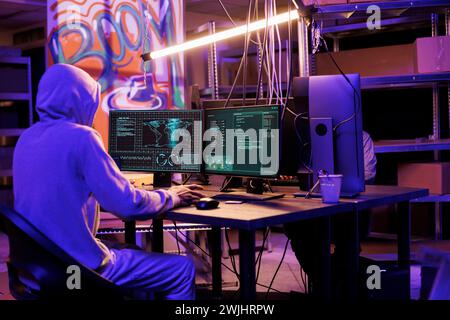 Hacker in hood gathering information using illegal spyware on computer to break into server. Criminal doing web tracking with malicious software and checking data on screen Stock Photo