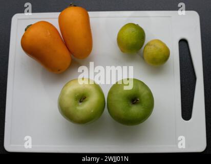 Closeup of two coconas, two limes and two green apples on a white cutting board with a dark background Stock Photo