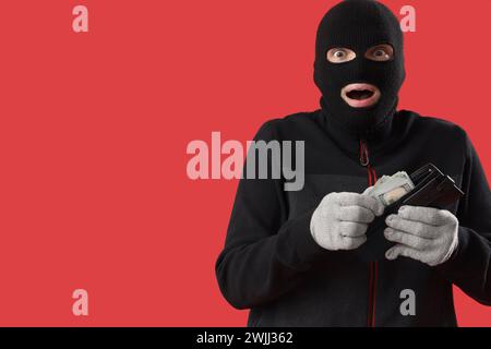 Shocked male burglar with wallet of money on red background Stock Photo