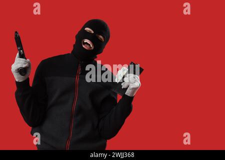 Happy male burglar with gun and money on red background Stock Photo