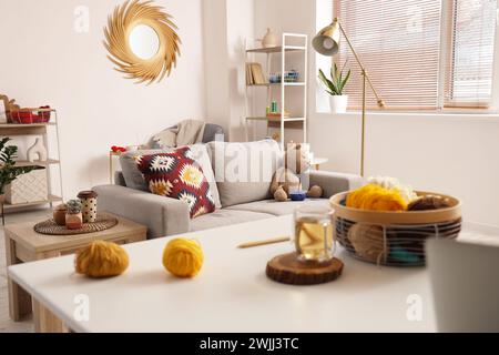 Knitted toy bear with yarn on sofa in living room interior Stock Photo