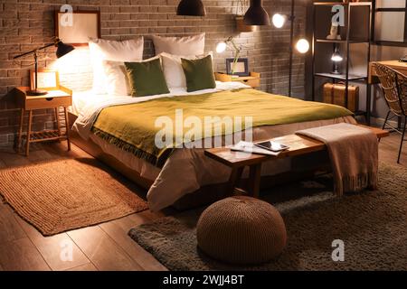 Interior of stylish bedroom with green blanket on bed and glowing lamps at night Stock Photo