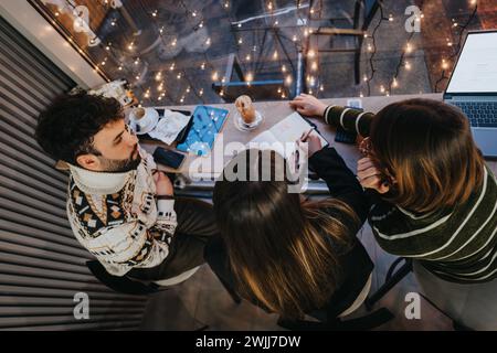 A dynamic scene of young individuals engaging in teamwork around a table, with a laptop and notes, under cozy festive lights. Stock Photo