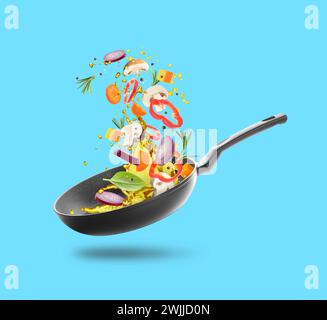 Different vegetables, oil, frying pan in air on light blue background Stock Photo