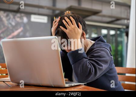 A stressed and upset young Asian woman is feeling overworked and tired while working remotely at a cafe. no passion, exhausted, worried about deadline Stock Photo