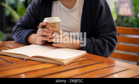 A cropped shot of a woman in casual clothes sipping coffee and writing down her ideas in a book while sitting in a cafe. keeping diary, jotting down, Stock Photo