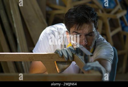 A man is focused as he shapes a piece of wood with his tools in a workshop setting. Stock Photo