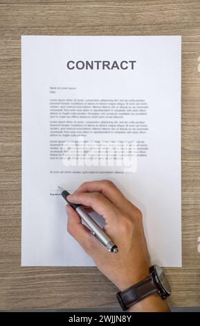 Closeup man hand holding a pen signing his name on a CONTRACT document. Top View Stock Photo