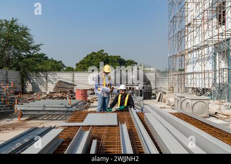 Two construction workers are working on construction tasks in front of a large building site with helmet and safety gear. Stock Photo