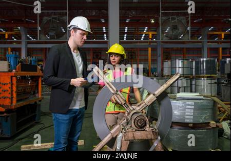 Two people wearing hard hats standing next to a large roll forming machine wheel in an industrial factory. Stock Photo