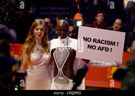 Berlin, Germany. 15th Feb, 2024. Papis Loveday (r) stands on the opening night of the Berlinale with a protest sign 'No Racism ! No AFD !' next to actress Pheline Roggan on the red carpet. The film 'Small Things Like These' is being shown. The 74th Berlin International Film Festival will take place from February 15 - 25, 2024. Credit: Monika Skolimowska/dpa/Alamy Live News Stock Photo
