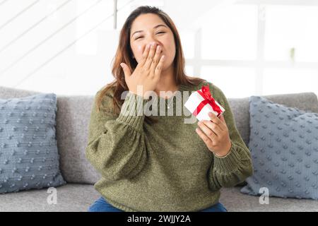 Young biracial woman looks surprised at home, holding a gift on a video call Stock Photo