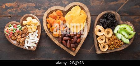 Healthy sweet dried fruits and berries in wooden heart shaped plates on wooden background. Stock Photo