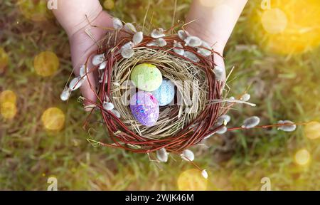 Hands holding decorated easter eggs in a small nest. Selective focus Stock Photo