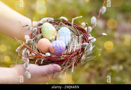 Hands holding decorated easter eggs in a small nest. Selective focus Stock Photo