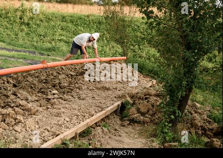 A plumber installs a reinforced orange sewer pipe during site maintenance. Stock Photo