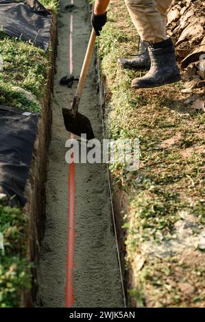 A plumber installs a reinforced orange sewer pipe during site maintenance. Stock Photo