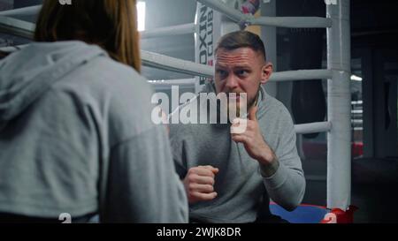 Male coach consults with female boxer in visible pain during a break in ...