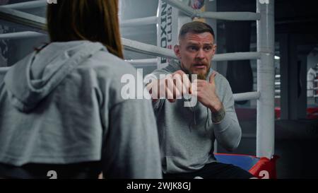 Male coach consults with female boxer in visible pain during a break in ...