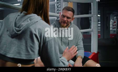 Male coach consults with female boxer in visible pain during a break in ...