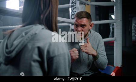 Male coach consults with female boxer in visible pain during a break in ...