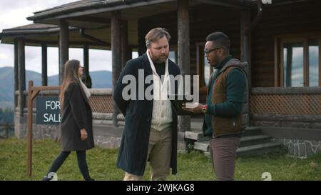 Family with kids visit potential home property. African American real state agent consults Caucasian man and shows plan of modern house on digital tablet computer. Residential property on sale concept Stock Photo