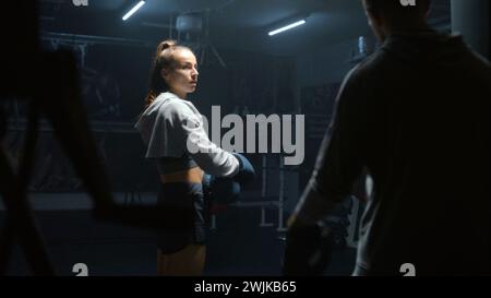 Athletic fighter in boxing gloves trains and exercises for fighting championship. Woman hits punching mitts and practices in fighting techniques with adult trainer. Physical activity and workout. Stock Photo